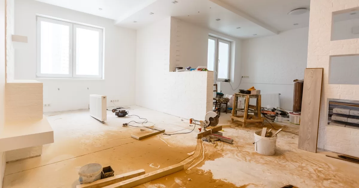A modern home interior is under renovation with supplies and power tools scattered throughout. Sawdust covers the floor.