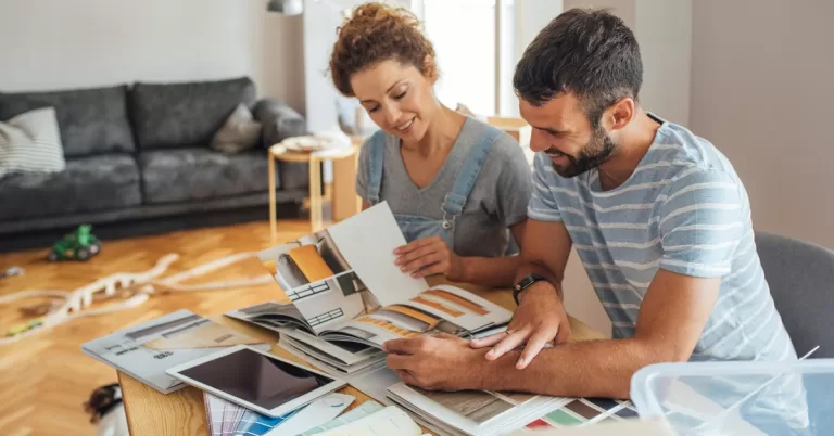 A couple sitting at a table in their home with several booklets and samples of materials for a home renovation.