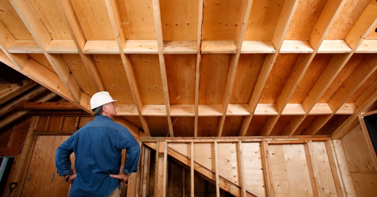 A man looks up at a structure under construction. The wooden structure features walls, stairs, and a door.