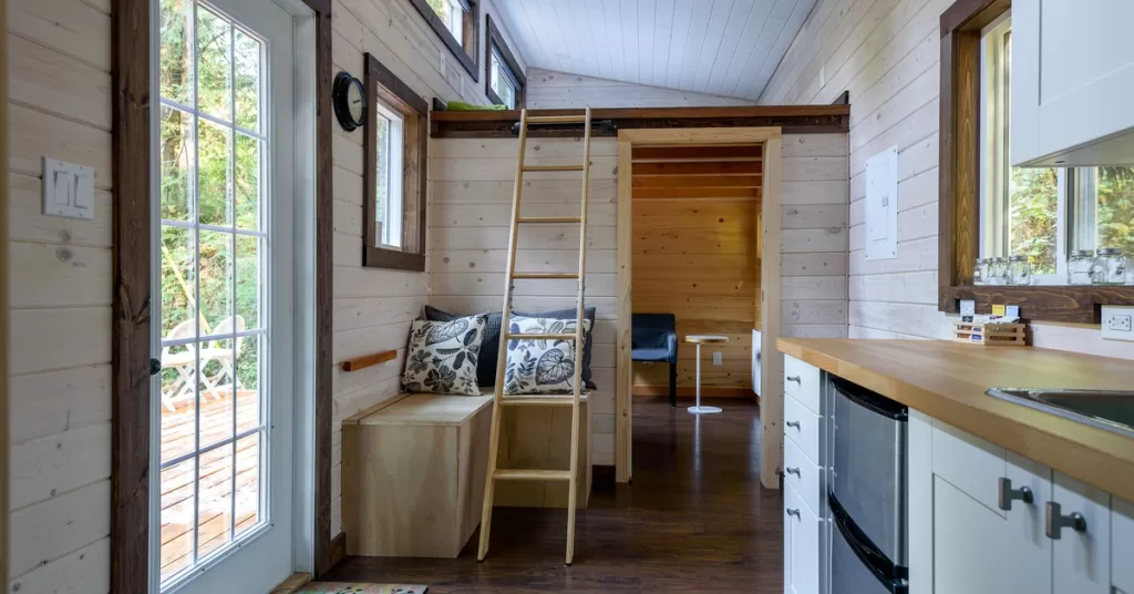 A small dining room with wood paneling on the walls. A wooden ladder rests next to a doorway into a living space.