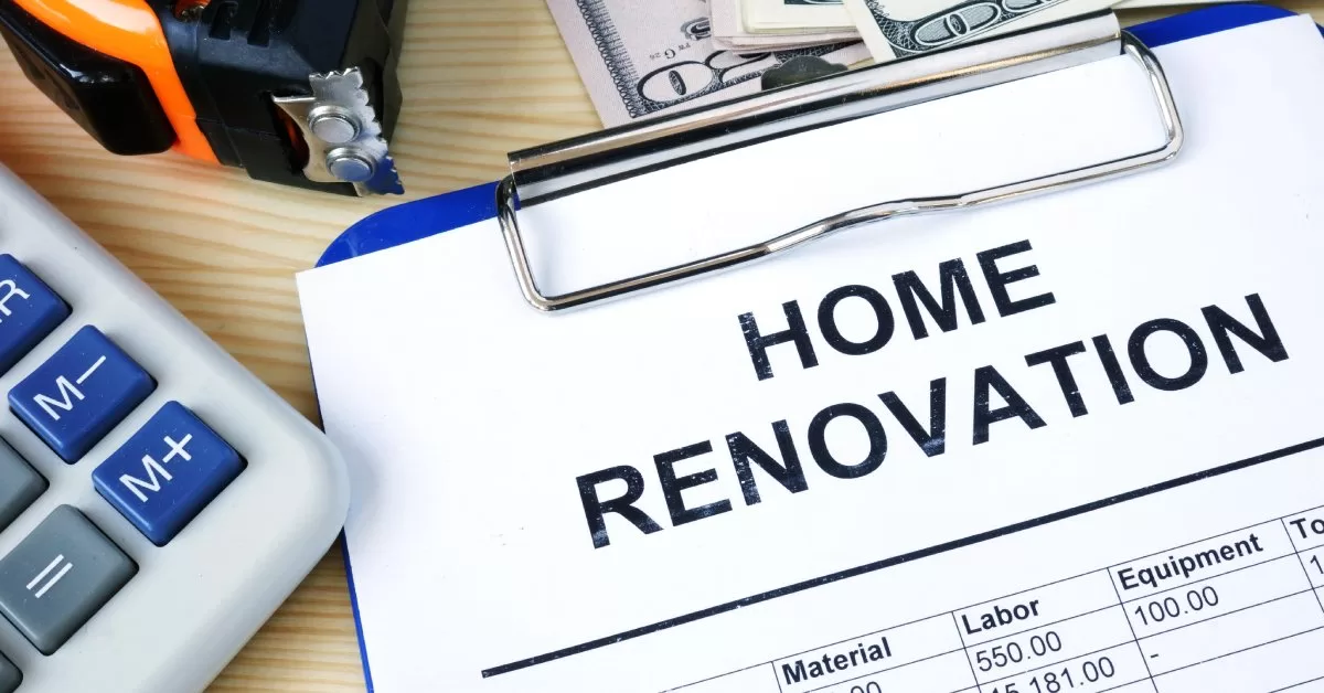 A blue clipboard holding a paper labeled "Home Renovation" next to a calculator, a small pile of cash, and a tape measure.