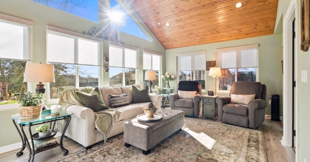 A bright open-concept living space with large windows, comfortable seating, and a wood-paneled ceiling.